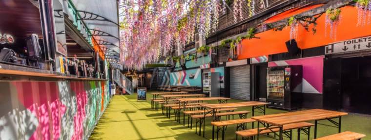 The Garden at Vauxhall Arches — covered walkway hung with blossom, lined with benches and food traders