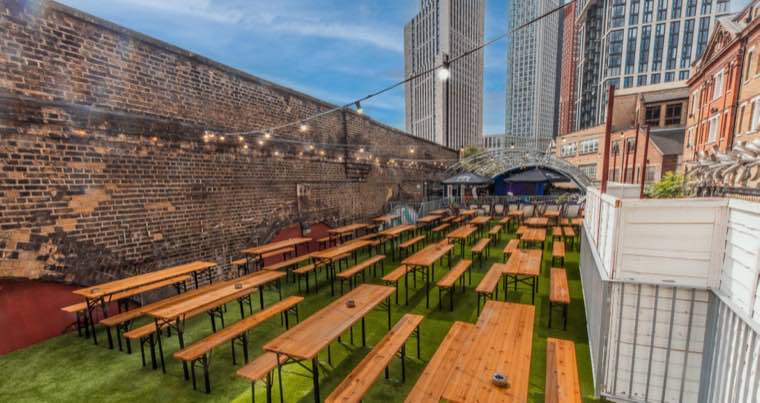Open-air terrace with long benches against a brick railway arch wall